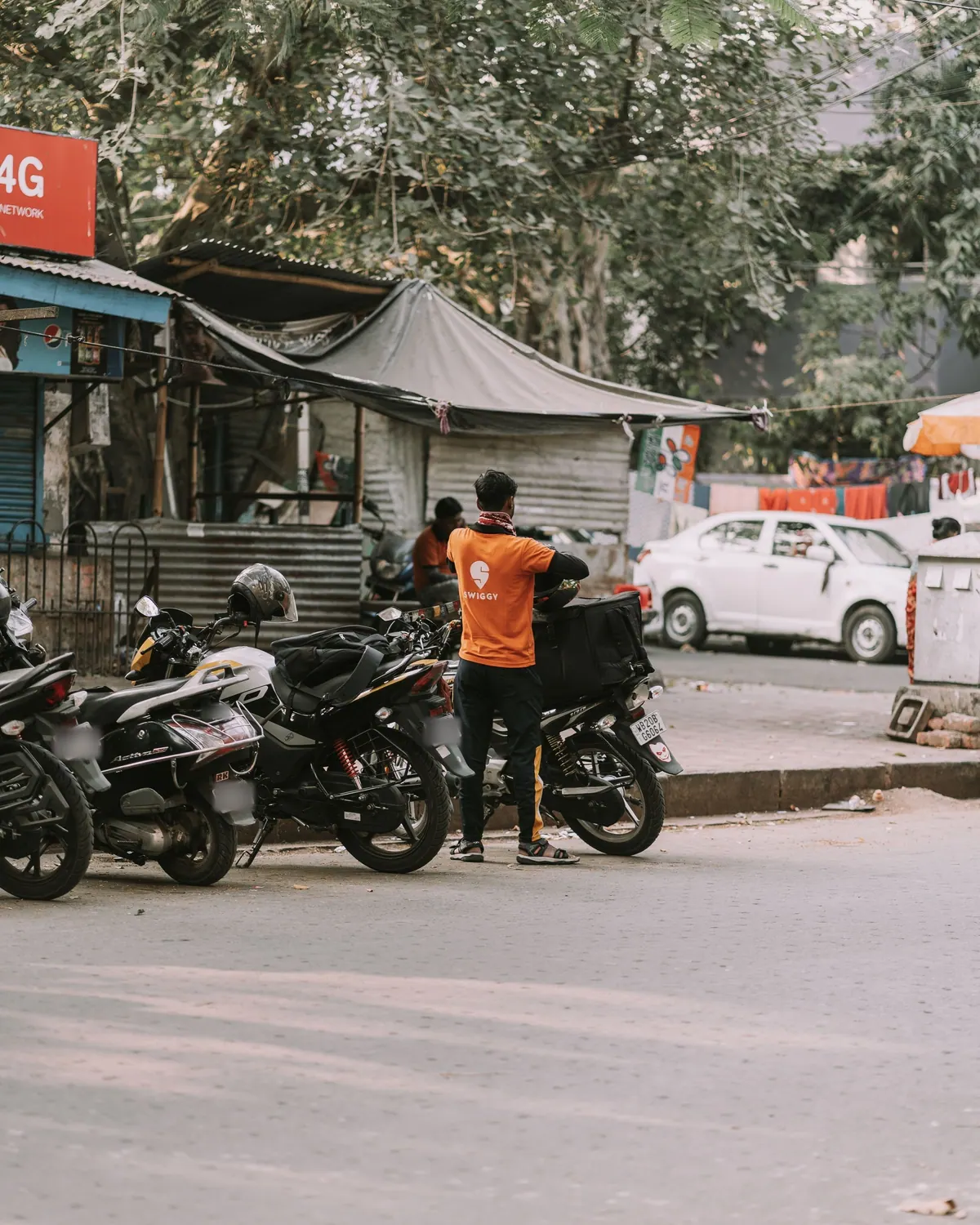 A delivery rider standing by a row of parked motorcycles on a city street