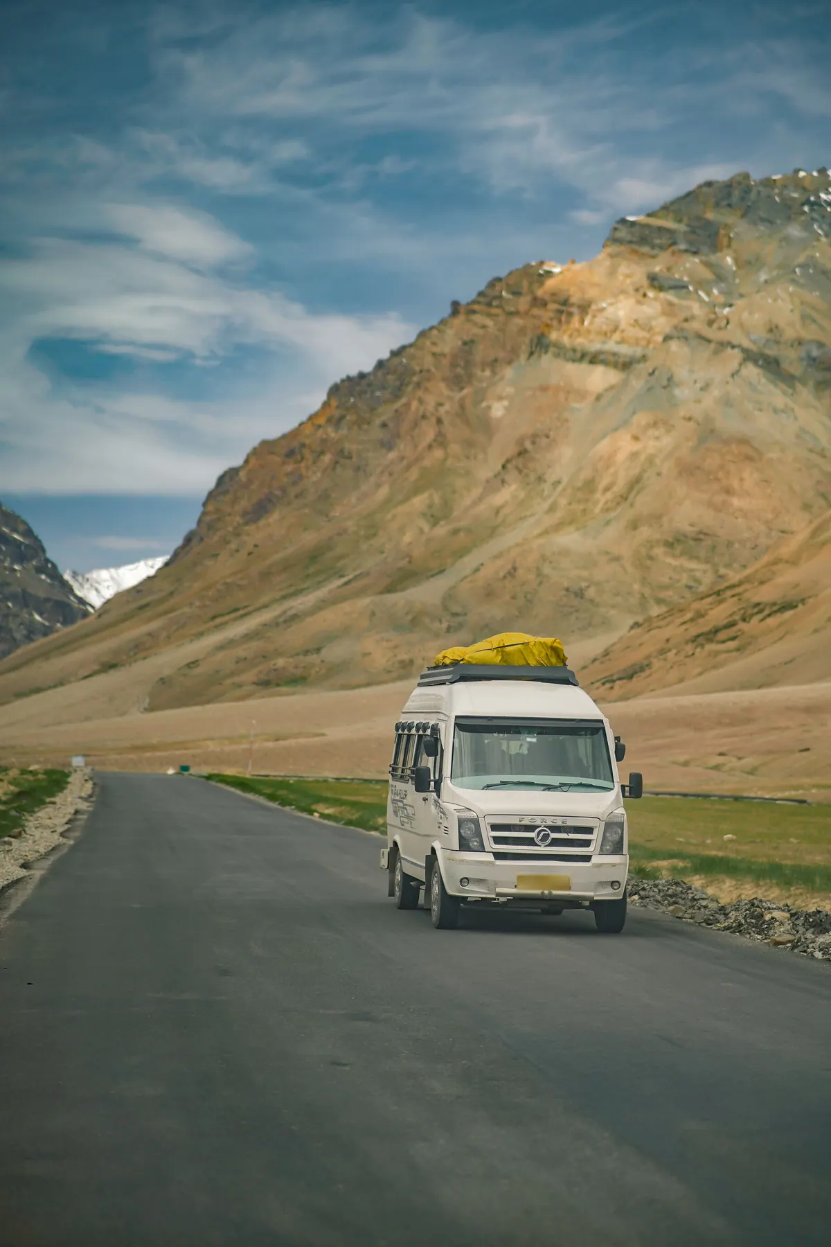 A white passenger van with luggage on its roof driving a mountain road